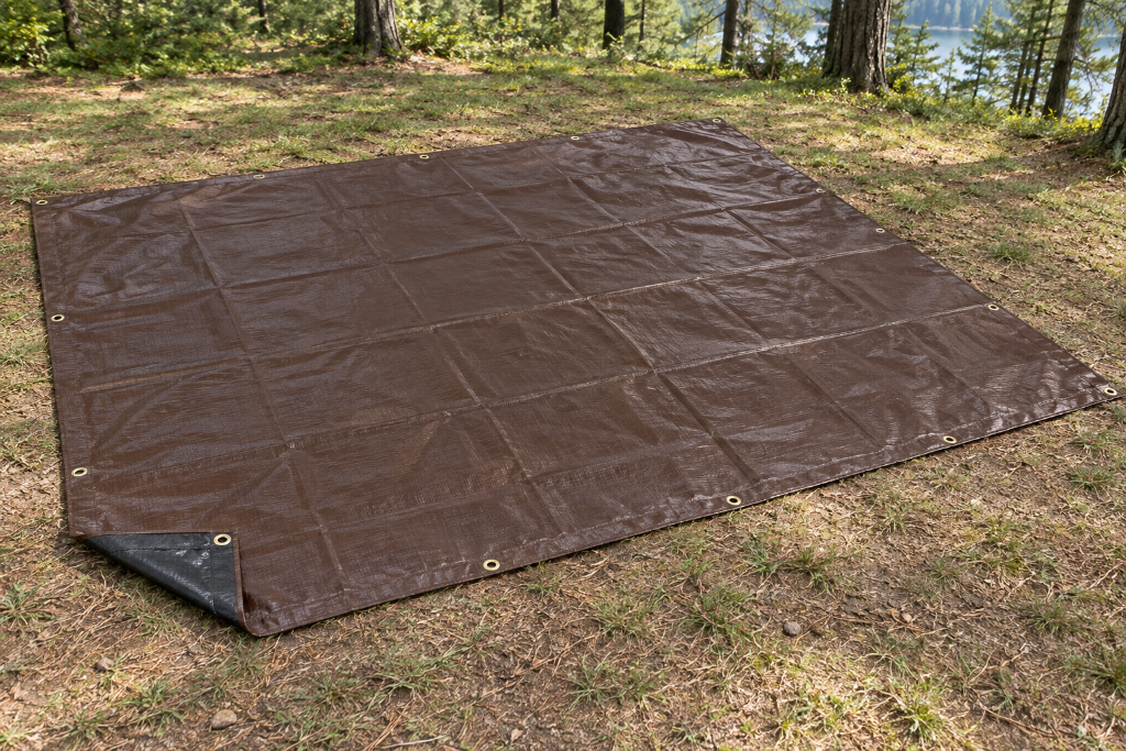 Heavy-duty brown tarp beneath a tent and protecting camping gear from wet ground.