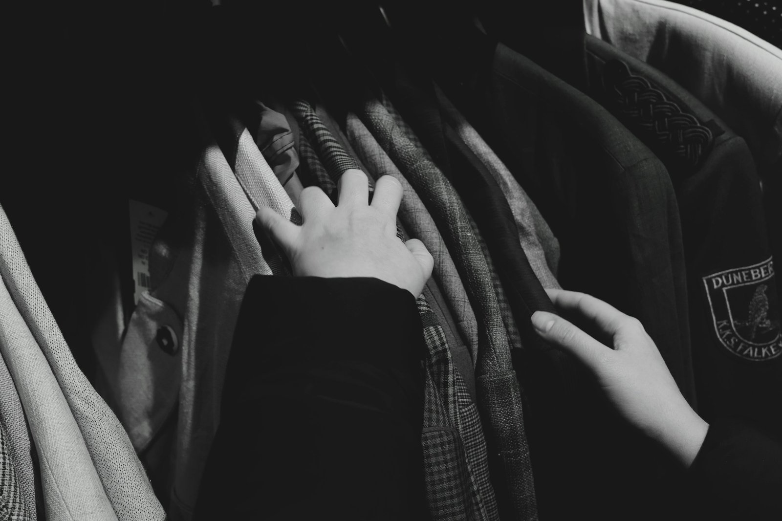 A shopper's hands moving along a rack of hanging clothes in a store.